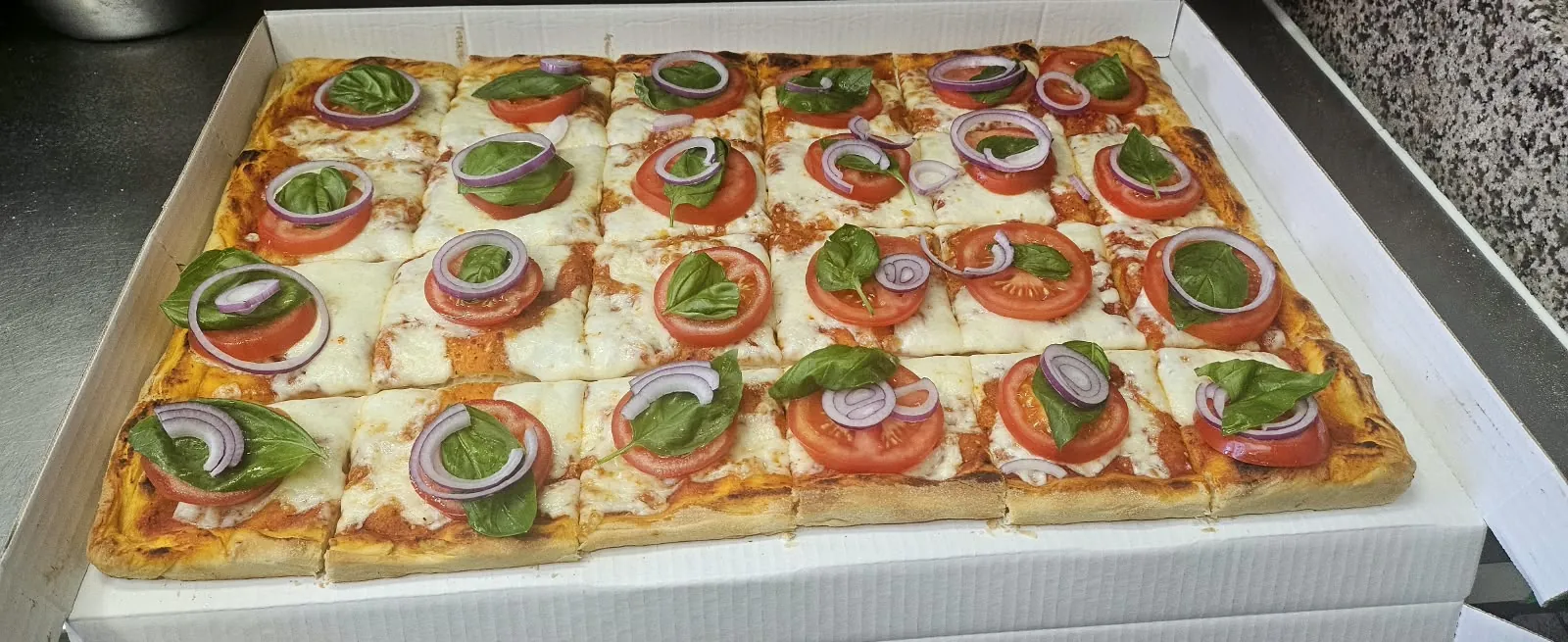 Blechpizza mit Tomatenscheiben, roten Zwiebeln, Basilikum und Mozzarella
